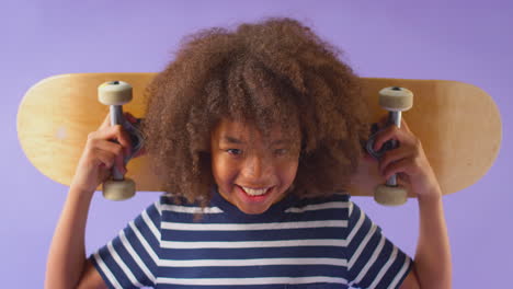 Studio-Shot-Of-Young-Boy-Holding-Skateboard-Across-Shoulders--Against-Purple-Background
