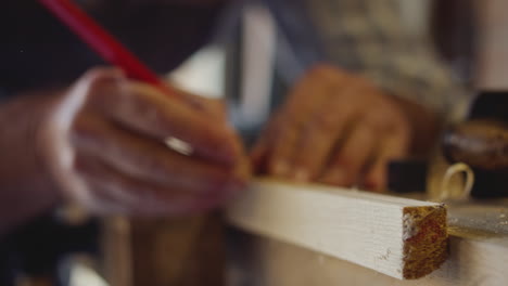 Close-Up-Of-Male-Carpenter-In-Garage-Workshop-Measuring-And-Planing-Piece-Of-Wood