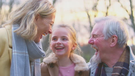 Portrait-Of-Grandparents-With-Granddaughter-Outside-Walking-Through-Winter-Countryside