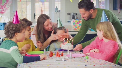 Mädchen-Bläst-Kerzen-Auf-Geburtstagstorte-Auf-Einer-Party-Mit-Eltern-Und-Freunden-Zu-Hause-Aus