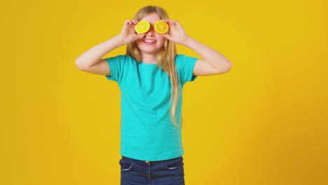 Studioporträt-Eines-Mädchens,-Das-Vor-Gelbem-Hintergrund-Zwei-Orangefarbene-Hälften-Vor-Augen-Hält