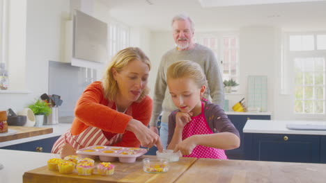 Großeltern-Und-Enkelin-Haben-Spaß-Daran,-Hausgemachte-Kuchen-Auf-Der-Küchentheke-Zu-Dekorieren