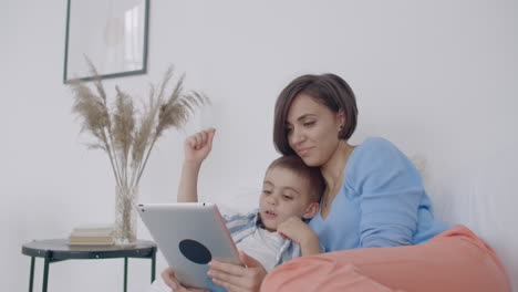 Mother-and-son-using-digital-tablet-in-bedroom-at-home.-Front-view-of-happy-Caucasian-mother-and-son-using-digital-tablet-in-bedroom-at-home