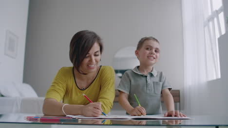 Mom-and-son-sitting-at-the-mirror-table-in-the-white-room-draw-with-colored-pencils-smiling-and-laughing