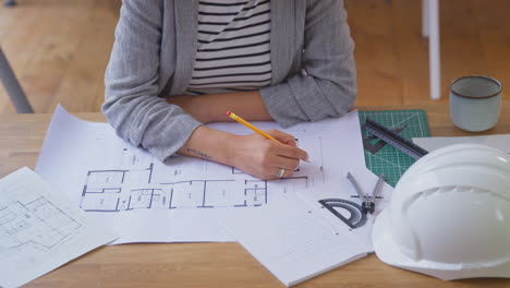 Close-Up-Of-Female-Architect-In-Office-At-Desk-Working-On-Plans-For-New-Building-With-Builder