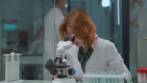 Expertos-En-Laboratorio-Científico-Mujer-Científica-Está-Investigando-Muestras-En-Microscopio-Explorando-El-Coronavirus-Y-Buscando-Una-Cura