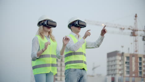 Two-managers-of-the-future-on-the-construction-site-use-virtual-reality-glasses-on-the-background-of-buildings-and-cranes-move-their-hands-and-click-on-the-icons.