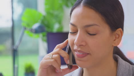 Close-Up-Of-Businesswoman-Working-In-Office-Sitting-At-Desk-Talking-On-Mobile-Phone
