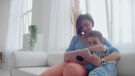 Mutter-Und-Sohn-Nutzen-Tablet,-Schauen-Auf-Den-Bildschirm-Und-Unterhalten-Sich-Auf-Dem-Sofa-In-Einem-Gemütlichen-Haus