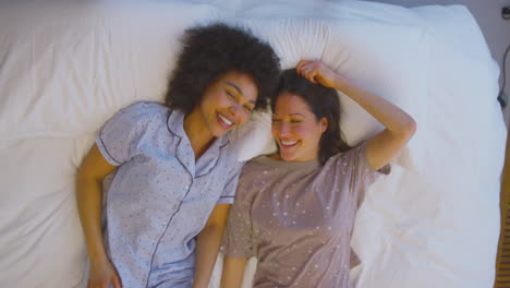 Overhead-Portrait-Shot-Of-Loving-Same-Sex-Female-Couple-Wearing-Pyjamas-Lying-On-Bed-At-Home