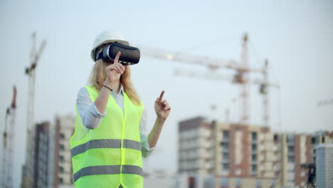 Portrait-of-a-female-inspector-analyzing-the-work-of-builders-using-virtual-reality-glasses-A-woman-in-a-helmet-and-a-protective-vest-stands-in-VR-glasses-and-moves-his-hands