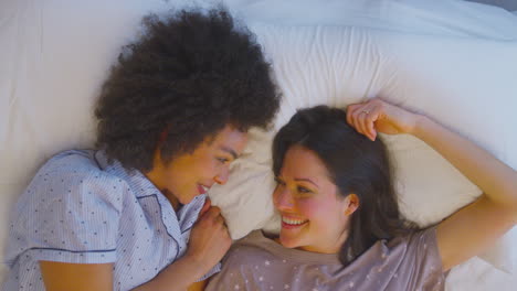 Overhead-Shot-Of-Loving-Same-Sex-Female-Couple-Wearing-Pyjamas-Lying-On-Bed-At-Home