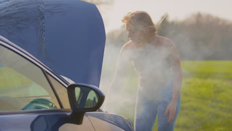 Woman-Broken-Down-On-Country-Road-Looking-Under-Smoking-Bonnet-Of-Car