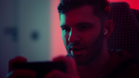 video-game-addiction-closeup-portrait-of-gamer-with-smartphone-in-room-at-night-young-man-playing-game-in-mobile-app-online-red-and-green-lights