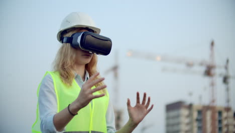 Portrait-of-a-female-crane-operator-operating-a-construction-site-using-virtual-reality-glasses-Woman-Construction-Manager-manages-the-progress-and-plan-of-buildings-using-gestures-at-sunset