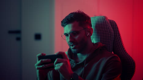 Happy-gamer-wear-headphone-competition-play-video-game-online-with-smartphone-colorful-neon-lights-in-living-room-at-home.-Esport-streaming-game-online-Home-quarantine-activity-concept.-High-quality-4k-footage