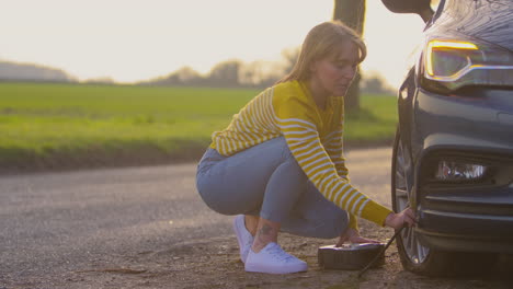 Woman-Inflating-Car-Tyre-With-Electric-Pump-On-Country-Road
