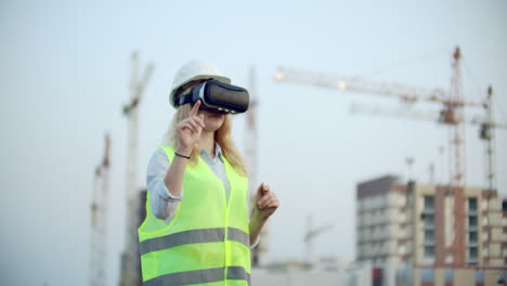 Portrait-of-a-female-crane-operator-operating-a-construction-site-using-virtual-reality-glasses.-Woman-Construction.-Manager-manages-the-progress-and-plan-of-buildings-using-gestures-at-sunset