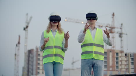 Two-managers-of-the-future-on-the-construction-site-use-virtual-reality-glasses-on-the-background-of-buildings-and-cranes-move-their-hands-and-click-on-the-icons.