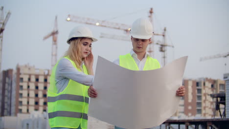 Woman-talking-on-the-phone-and-asks-the-Builder-what-is-on-the-drawings-standing-on-the-background-of-buildings-under-construction.
