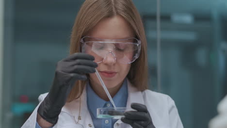 student-of-chemical-institute-is-doing-practical-work-in-class-portrait-of-young-woman-with-protective-glasses-rubber-gloves-and-white-gown-exploring-reagent