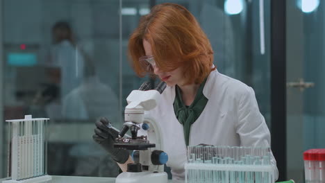 red-haired-woman-virologist-is-researching-virus-of-covid-19-in-medical-laboratory-viewing-it-in-microscope-exploring-coronavirus-and-looking-for-a-curing