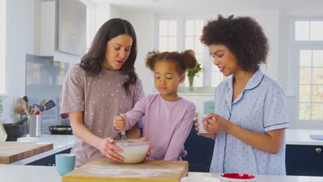 Familie-Mit-Zwei-Müttern-Im-Schlafanzug,-Die-Zu-Hause-Mit-Ihrer-Tochter-Morgenpfannkuchen-In-Der-Küche-Backen