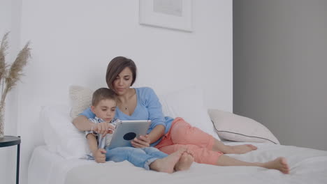 Mutter-Und-Sohn-Benutzen-Ein-Digitales-Tablet-Im-Schlafzimmer-Zu-Hause.-Vorderansicht-Einer-Glücklichen-Kaukasischen-Mutter-Und-Ihres-Sohnes,-Die-Ein-Digitales-Tablet-Im-Schlafzimmer-Zu-Hause-Benutzen