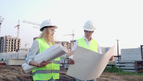 Workers-with-drawings-at-the-construction-site.-Two-workers-man-and-woman-in-protective-harhats-working-with-drawings-at-the-construction-site-outdoors.
