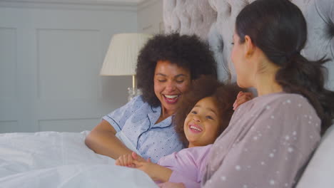 Family-With-Two-Mums-Wearing-Pyjamas-In-Bed-At-Home-With-Daughter