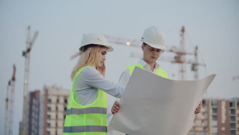 Two-engineers-discuss-looking-at-the-drawings-of-the-construction-plan-and-the-location-of-the-objects-specifying-the-contractor-on-the-phone-details.-Talking-on-the-phone-at-the-construction-site.