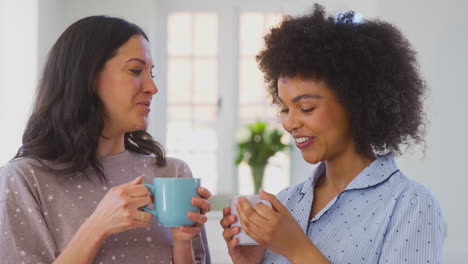 Loving-Same-Sex-Female-Couple-Wearing-Pyjamas-Drinking-Morning-Coffee-In-Kitchen-At-Home