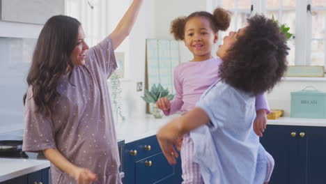 Pregnant-Family-With-Two-Mums-Dancing-Making-Morning-Pancakes-In-Kitchen-With-Daughter