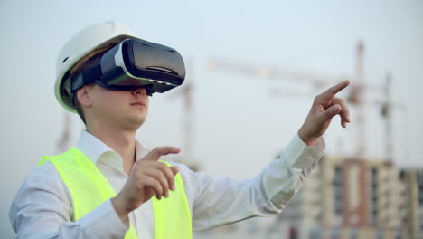 Portrait-of-a-male-crane-operator-operating-a-construction-site-using-virtual-reality-glasses.-Construction-Manager-manages-the-progress-and-plan-of-buildings-using-gestures-at-sunset