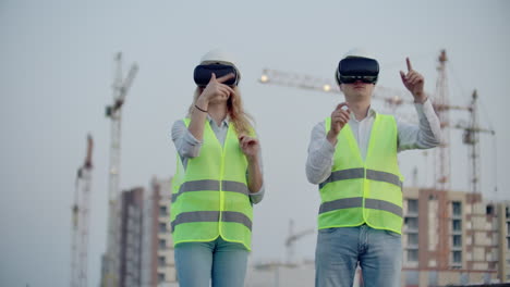 Two-people-Man-and-woman-wearing-virtual-reality-glasses-on-the-background-of-buildings-under-construction-with-cranes.-Manager-and-assistant-on-design-with-your-hands-mimicking-the-interface-of-the-application