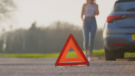 Hazard-Warning-Triangle-Sign-For-Car-Breakdown-On-Road-With-Woman-Calling-For-Help