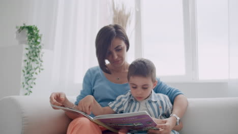 Portrait-of-little-cute-boy-reading-book-with-mother-while-sitting-on-safe