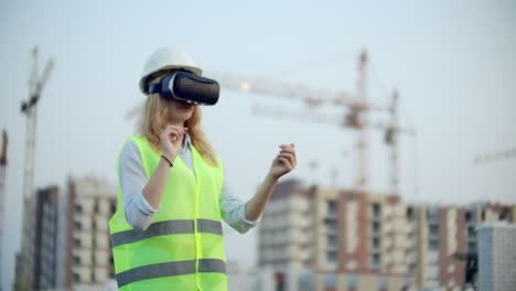 Portrait-of-a-female-crane-operator-operating-a-construction-site-using-virtual-reality-glasses.-Woman-Construction-Manager-manages-the-progress-and-plan-of-buildings-using-gestures-at-sunset