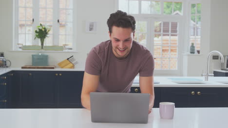 Transgender-Man-Working-From-Home-Looking-At-Laptop-On-Kitchen-Counter