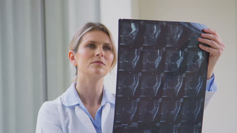 Female-Doctor-Wearing-White-Coat-Standing-In-Hospital-Corridor-Looking-At-CT-Or-MRI-Scan