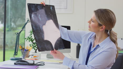 Woman-Doctor-Or-GP-Sitting-At-Desk-In-Office-Looking-At-CT-Or-MRI-Scan