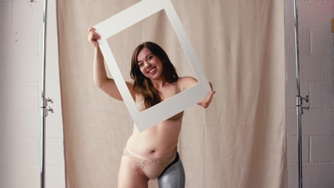 Studio-Shot-Of-Confident-Woman-With-Prosthetic-Limb-In-Underwear-Looking-Through-Picture-Frame