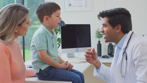 Male-Doctor-Or-GP-Wearing-White-Coat-Examining-Boy-Looking-At-Mouth-And-Throat