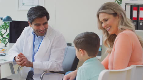 Smiling-Doctor-Or-GP-In-White-Coat-Meeting-Mother-And-Son-For-Appointment-In-Office