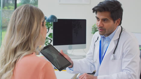 Arzt-Im-Weißen-Kittel-Im-Büro,-Der-Einer-Reifen-Patientin-Eine-Röntgenaufnahme-Oder-Einen-Scan-Auf-Einem-Digitalen-Tablet-Zeigt