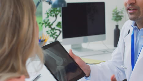Arzt-Im-Weißen-Kittel-Im-Büro,-Der-Einer-Reifen-Patientin-Eine-Röntgenaufnahme-Oder-Einen-Scan-Auf-Einem-Digitalen-Tablet-Zeigt