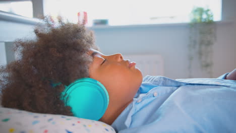 Niño-Acostado-En-La-Cama-Usando-Auriculares-Inalámbricos-Con-Los-Ojos-Cerrados-Escuchando-Música-O-Audiolibro