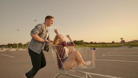Cheerful-people-a-couple-a-man-and-a-woman-at-sunset-ride-on-supermarket-trolleys-in-slow-motion.