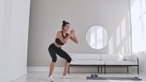 Woman-exercising-jumping-squats-in-home.-Healthy-female-in-sportswear-doing-jumping-squats-at-home.-Woman-exercising-at-living-room