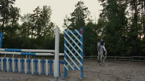Young-female-rider-on-bay-horse-jumping-over-hurdle-on-equestrian-sport-competition